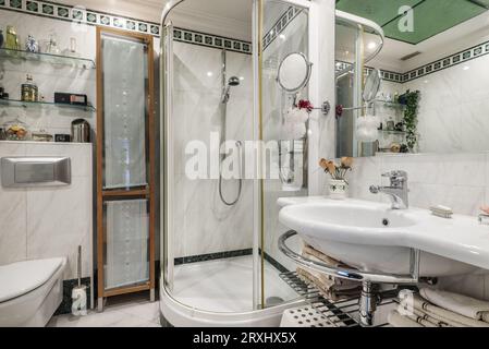 a bathroom with a one-piece porcelain sink under a frameless mirror and next to a curved shower stall Stock Photo