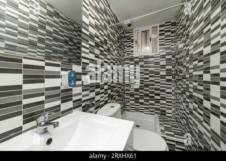 a bathroom with a one-piece porcelain sink beneath a frameless mirror and next to a curtainless shower stall and dizzying tiles Stock Photo