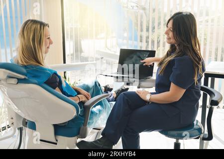 Doctor explains to her patient the digital X-ray images on a computer in the dental office. Stock Photo