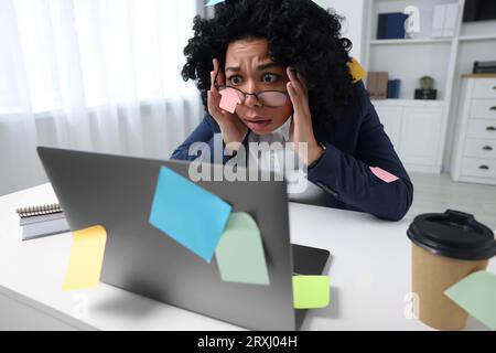 Deadline concept. Stressed woman looking at laptop in office. Many sticky notes everywhere as reminders Stock Photo