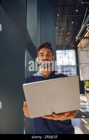 Handsome entrepreneur working on laptop standing in coworking during working day and looks camera Stock Photo