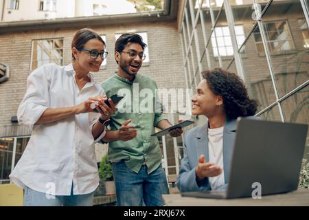 Cheerful coworkers discuss the project while use laptop on cafe terrace background Stock Photo