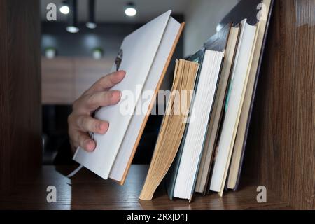 Hand of male selecting a book from bookshelf. The guy chooses a book to read from the shelf Stock Photo