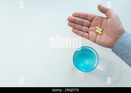 White pills of painkiller or antibiotic for treatment on senior man hand palm on a white background, glass with water, medicines and vitamin supplemen Stock Photo