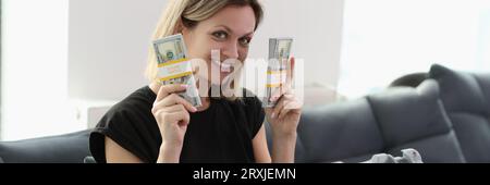 Smiling woman with suitcase full of money holding stacks of dollar bills and looking at camera. Stock Photo