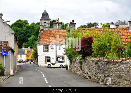 Vintage sports car parked beside a white stone building with a red tile roof along a narrow roadway in the historic village of Culross, Fife, Scotland Stock Photo