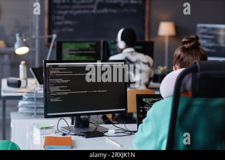Rear view of young people sitting at their workplaces with computers and working with program Stock Photo