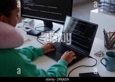 Programmer sitting at her workplace with computers and writing codes on laptop in office Stock Photo