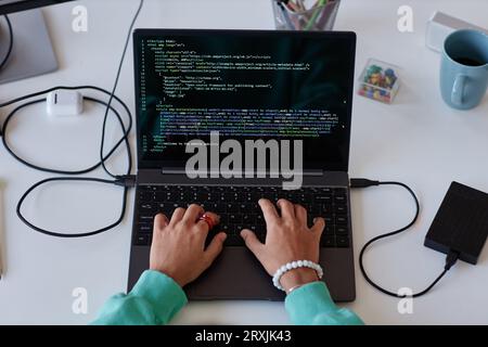 Top view of young woman writing computer codes on laptop while sitting at her workplace Stock Photo