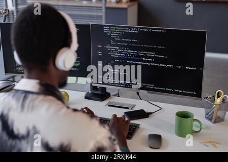 Rear view of programmer in headphones typing codes on computer while working in IT office Stock Photo