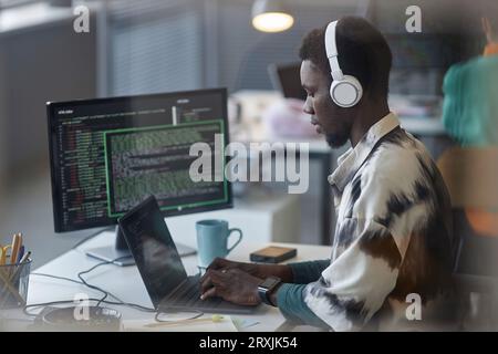 African American programmer in headphones typing on laptop at his workplace Stock Photo