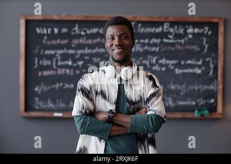 Portrait of African American teacher smiling at camera while standing with his arms crossed with blackboard in background Stock Photo