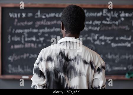 Rear view of African American man reading information on blackboard standing in the classroom Stock Photo