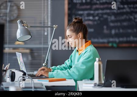 Young woman sitting at table and typing on laptop in office Stock Photo