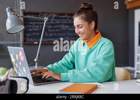 Young smiling woman working online on laptop while sitting at table in office Stock Photo