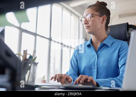 Low angle view of young businesswoman sitting at her workplace and working on computer in office Stock Photo