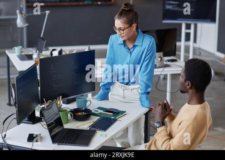 Young woman checking the computer codes of her colleague while he developing new software in office Stock Photo
