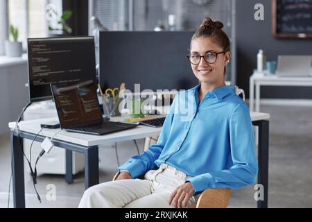 Portrait of young programmer in eyeglasses smiling at camera while sitting in IT office Stock Photo