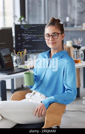 Portrait of young programmer in eyeglasses sitting in office and looking at camera while drinking coffee Stock Photo