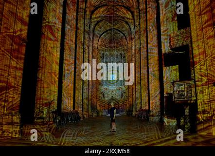 A lady views of the Nave at Canterbury Cathedral in Kent during a preview of the Luxmuralis: Renaissance, an art installation using moving light displays and original compositions to highlight the cathedral's architecture and immerse visitors in paintings and artwork from the Renaissance period during the Canterbury Festival. Picture date: Monday September 25, 2023. Stock Photo