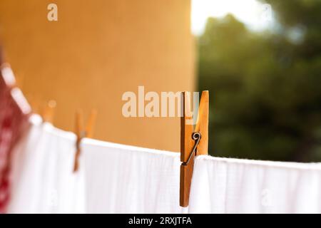 Blurred laundry colored clothes along with white hanging on clothesline while drying in sunlight and fastened with wooden clothespins against brown wa Stock Photo