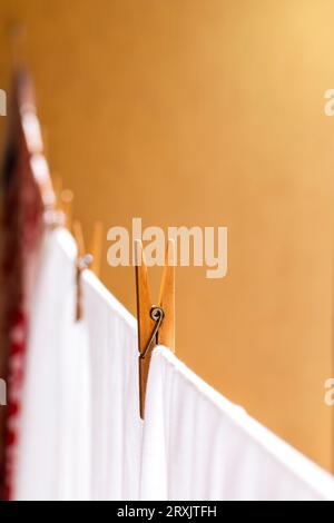 Blurred laundry colored clothes along with white hanging on clothesline while drying in sunlight and fastened with wooden clothespins against brown wa Stock Photo