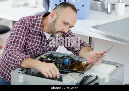 serviceman looking at tablet while repairing washing machine Stock Photo