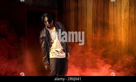 A scary zombie with blood and wounds on his body is walking in smoke with a wooden wall background. Scary zombie. Halloween concept Stock Photo