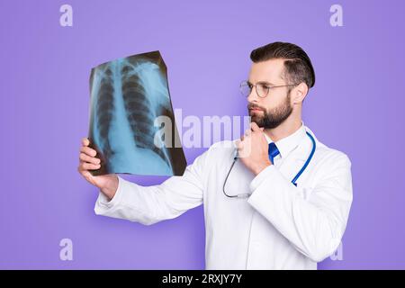 Portrait of pensive minded doc in white lab coat, uniform holding hand on chin looking at x-ray of lungs, trying to establish a diagnosis, isolated on Stock Photo