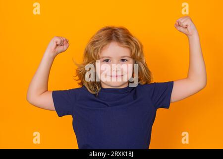 Cute child showing muscles on yellow studio isolated background. Power kids. Kid boy showing strong fists. Stock Photo