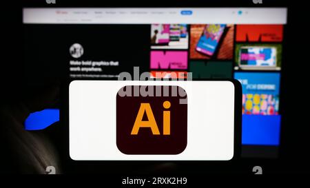 Person holding mobile phone with logo of vector graphics editor Adobe Illustrator on screen in front of company web page. Focus on phone display. Stock Photo