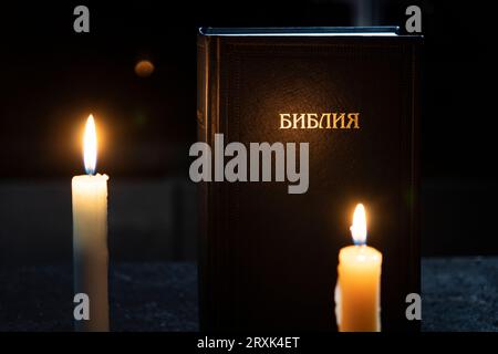 Holy Bible and two burning candles on the black table. The concept of faith and religion. christian faith. The inscription on the book translated from Stock Photo
