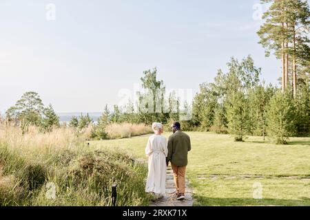 Rear view of senior couple holding hands and enjoying their walk in the park Stock Photo