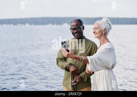 Senior couple making selfie portrait on the phone against the lake outdoors Stock Photo