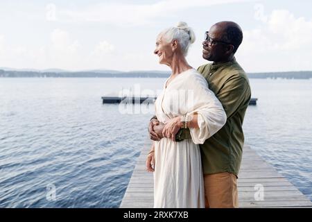 Senior man embracing his happy wife while they enjoying the view of the lake Stock Photo