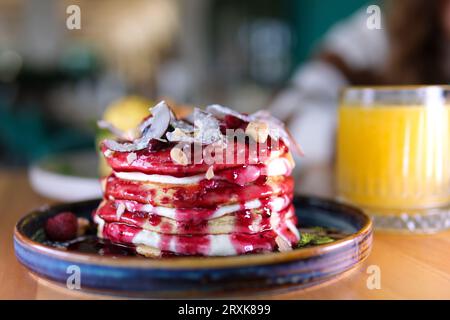 stack of delicious pancakes on blue plate in form of cake decorated with coconut flakes blueberries hazelnuts almond flakes raspberries and jam delicious breakfast with sour cream. eaten with fork Stock Photo