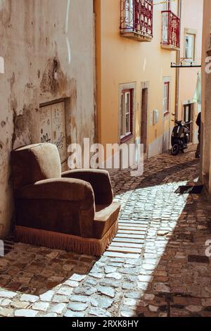 Abandoned old armchair on Lisbon street, Portugal. Retro brown armchair outside house. Vintage broken furniture. Narrow street with retro furniture Stock Photo