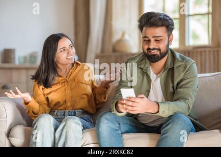 Furious indian wife scolding her dishonest husband using smartphone, woman looking for attention from boyfriend Stock Photo