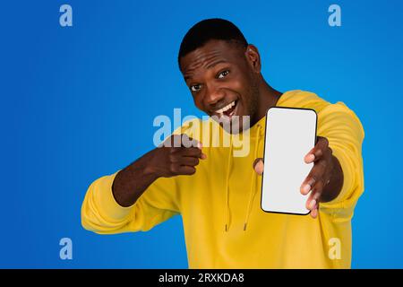 Smiling excited young black guy blogger pointing finger at camera, show phone with empty screen recommends website, sale Stock Photo