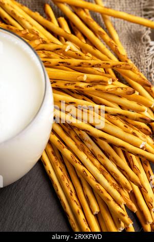 Thin and long bread sticks made of wheat flour and a glass of milk , sweet wheat pastries on the table with cow 's milk Stock Photo