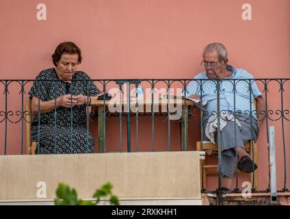 elderly retired couple sitting on a balcony together lady looking at mobile device and man reading the newspaper, older husband and wife relaxing. Stock Photo