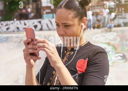 Young woman listening to music at skate park Stock Photo