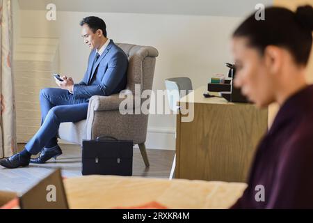Businessman using smart phone in hotel room armchair Stock Photo