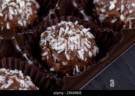 Chocolate candies in the form of balls with milk coconut filling sprinkled with coconut chips, delicious and soft chocolate coconut cakes of small siz Stock Photo