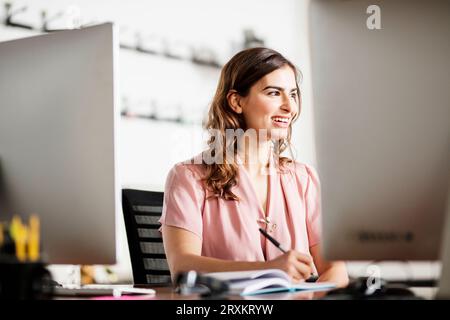 Smiling young businesswoman writing notes at desk Stock Photo