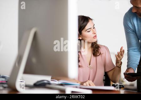 Young businesswoman talking to colleague at desk in office Stock Photo