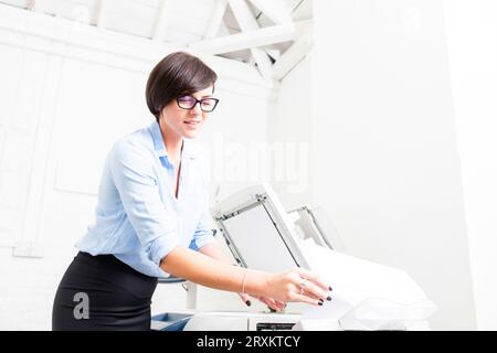 Businesswoman with glasses using photocopier in office Stock Photo