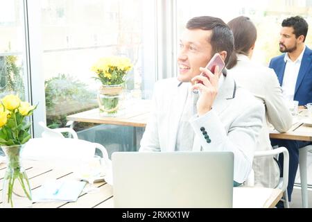 Businessman using smartphone by laptop in restaurant Stock Photo
