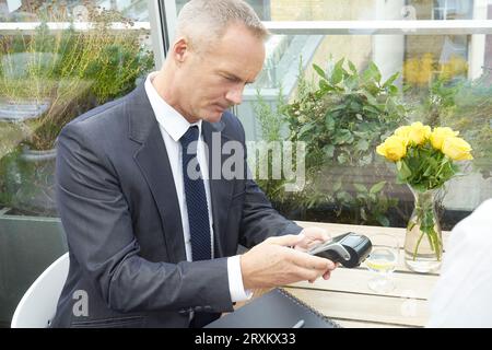 Businessman using EFTPOS machine at restaurant table Stock Photo