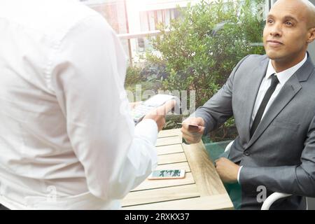 Businessman using EFTPOS machine at restaurant table Stock Photo
